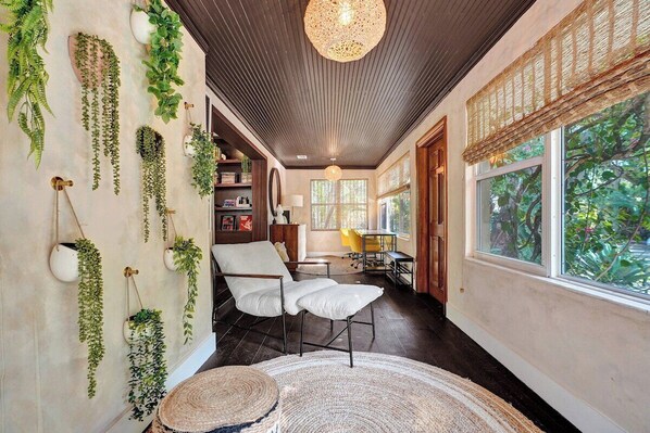 A room with a white chair, a woven rug, and hanging plants.