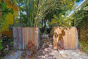 A pathway leading to a wooden gate, surrounded by lush greenery and a yellow building.