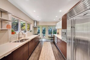 A modern kitchen with stainless steel appliances, wooden cabinets, and a view of greenery outside.