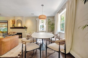 Un espace repas comprenant une table ronde et des chaises, un luminaire suspendu et une vue sur l’extérieur grâce à de grandes fenêtres.