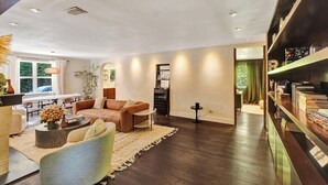 A modern living room with a sofa, coffee table, and bookshelves. - Luxury Morningside Bungalow Steps to the Park (Miami)