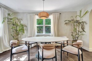 A dining area with a round table, six chairs, and two potted plants.