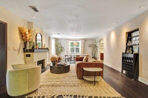 A spacious living room with a fireplace, a sofa, a coffee table, and a dining area in the background.