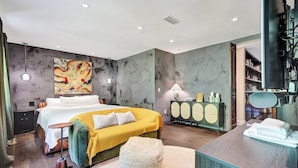 A modern hotel room with a large bed, a desk, a cabinet, and a painting on the wall. - Luxury Morningside Bungalow Steps to the Park (Miami)