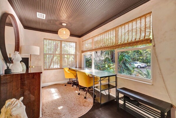 A modern office space with a desk, chairs, and a large window offering a view of greenery and a parked car.