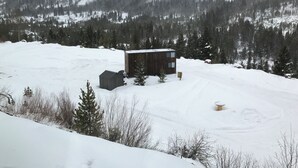 Una cabaña de madera con techo nevado, rodeada por un paisaje invernal y un bosque denso.