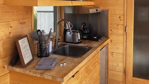 Una cocina compacta con paredes de madera, un lavamanos de acero inoxidable, una tetera y un microondas.