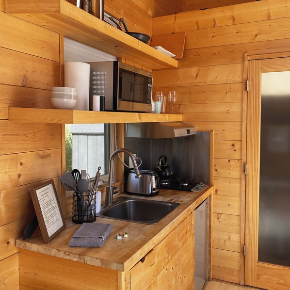 Una cocina compacta con paredes de madera, un lavamanos de acero inoxidable, una tetera y un microondas.