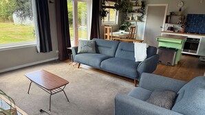 Ein Wohnzimmer mit einem blauen Sofa, einem Holztisch und Blick ins Freie durch große Fenster.