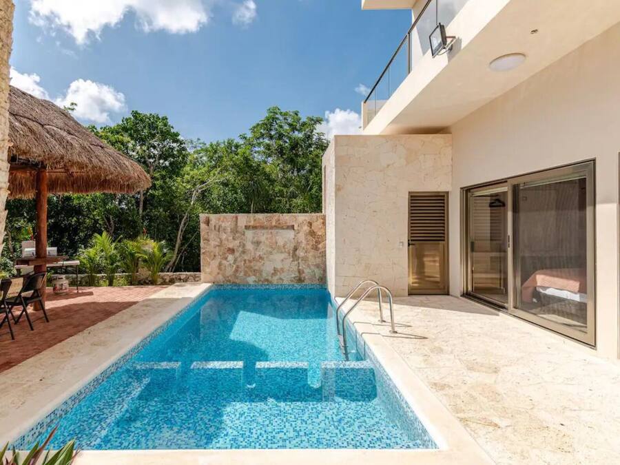 A modern outdoor swimming pool with a stone wall and a thatched-roof structure.