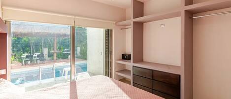 A bedroom with a large bed, a sliding glass door to a balcony, built-in shelving, and a small desk.