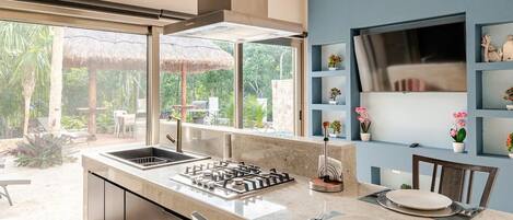 Una cocina moderna con una isla central, estufa integrada y un amplio ventanal con vistas a un jardín.