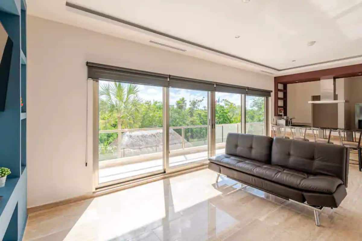 A modern living room with a leather sofa, large sliding glass doors, and a dining area with a table and chairs.