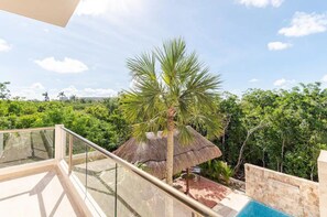 A balcony with a glass railing overlooking a lush garden and a pool area. - Tulum Country Home (Akumal)