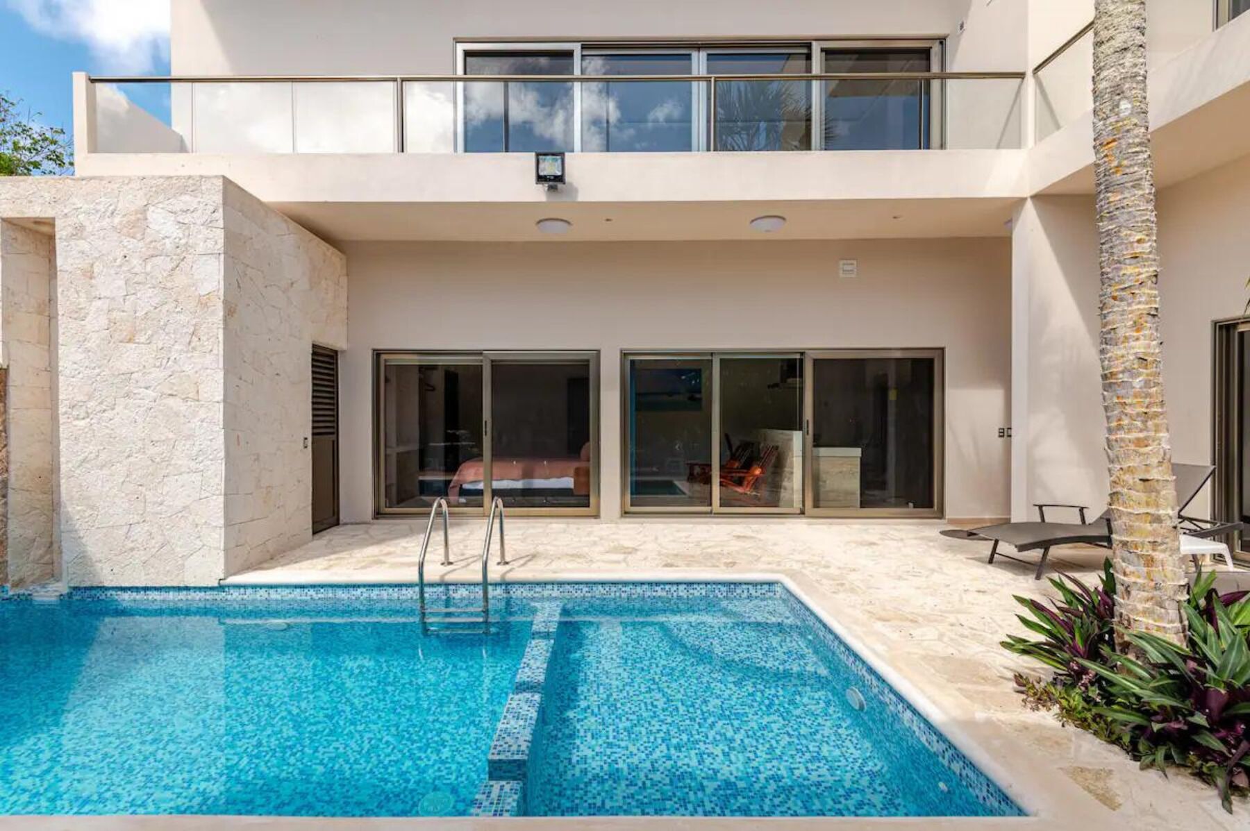 Une maison moderne dotée d’une piscine, de grandes portes vitrées et d’un balcon.