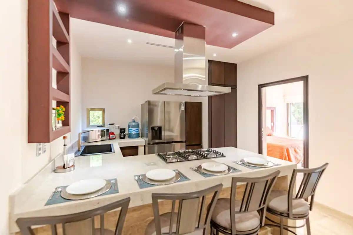 A modern kitchen with a central island, stainless steel appliances, and a dining area with four chairs.