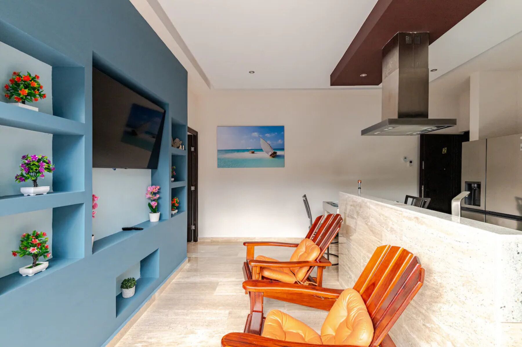 A modern living room with a blue accent wall, a wooden chair, a TV, and a painting of a sailboat.