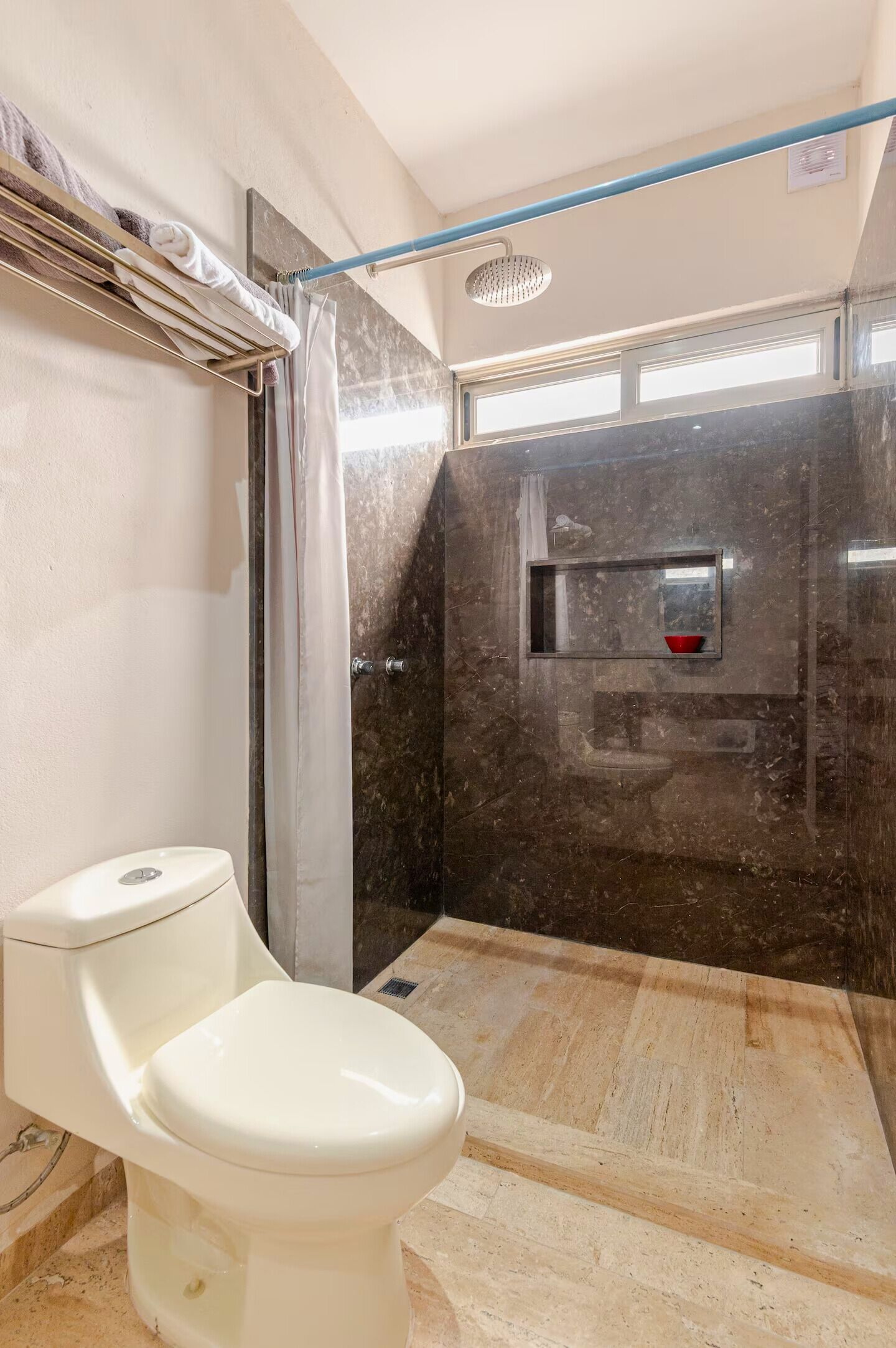A bathroom with a toilet, a shower with a glass door, and a marble floor.