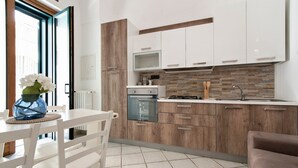 A modern kitchen with white cabinets, a wooden accent wall, a gas stove, and a dining area with a white table and chairs. - San Giusto 21 Old Town - Lecce Selection (Lecce)