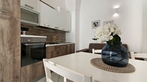 A modern kitchen with white cabinetry, a built-in oven, and a dining area with a white table and chairs. - San Giusto 21 Old Town - Lecce Selection (Lecce)