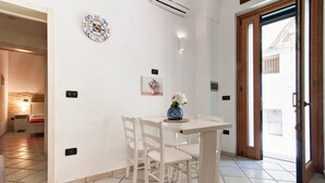 A dining area with a white table and chairs, a decorative clock, and a vase with flowers on the wall. - San Giusto 21 Old Town - Lecce Selection (Lecce)
