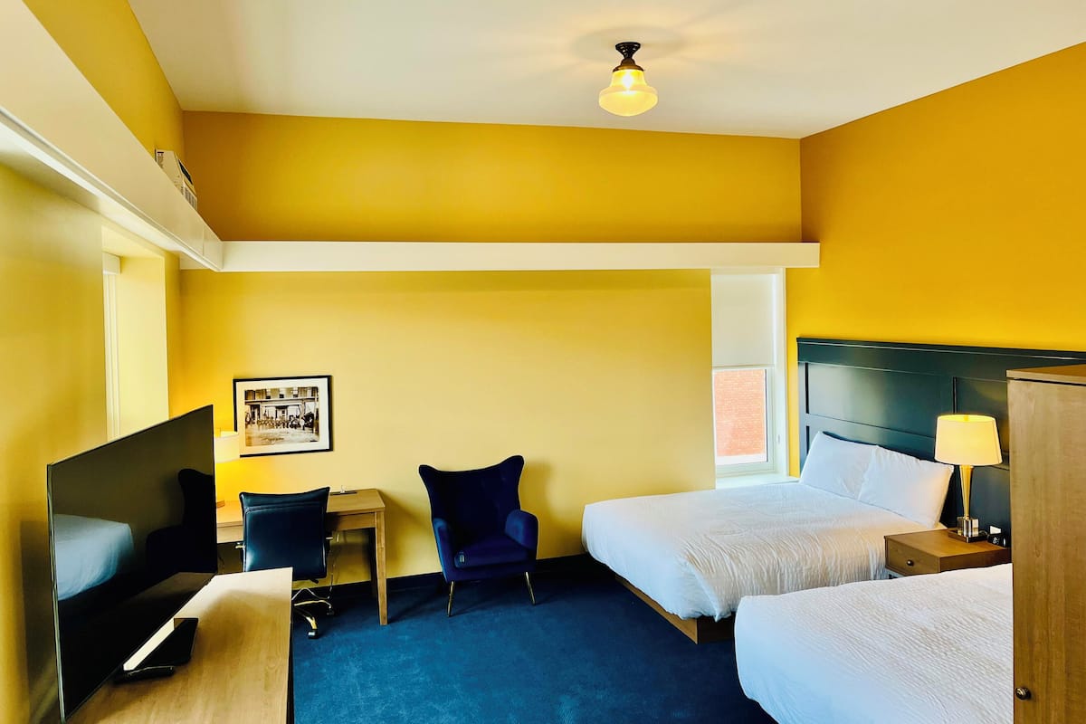 A hotel room with two beds, a desk with a chair, a TV, and a framed picture on the wall.