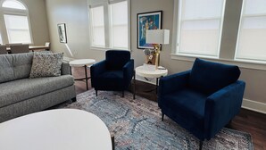 A modern living room with a grey sofa, two blue armchairs, a white coffee table, and a patterned rug.