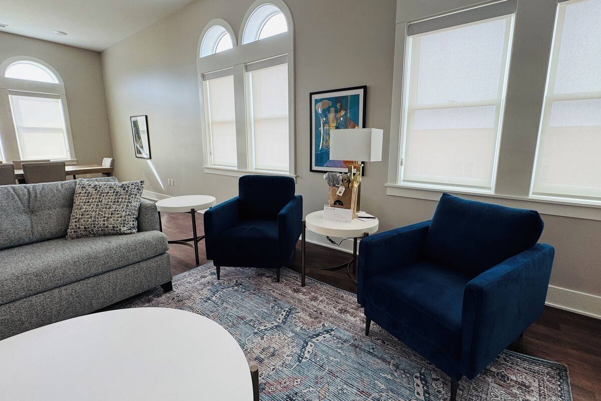 A modern living room with a grey sofa, two blue armchairs, a white coffee table, and a patterned rug.