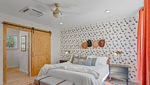 Une chambre à coucher comprenant un lit, des tables de chevet, un banc, un porte-chapeaux fixé au mur et une porte coulissante.
