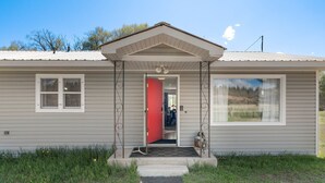 Une maison de plain-pied avec une porte rouge, un porche et un petit jardin à l’avant.