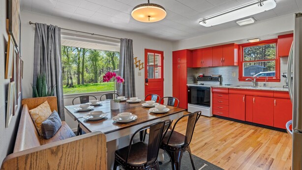 Une cuisine moderne avec des meubles rouges, une table à manger pour quatre personnes et une grande fenêtre donnant sur un paysage verdoyant.