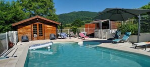 Ein Schwimmbecken mit Liegestühlen, eine Holzblockhütte und ein überdachter Bereich mit Sonnenschirm.