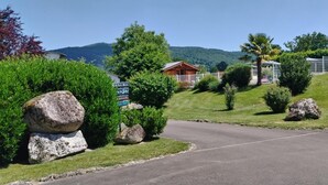 A rural setting with a wooden cabin, a paved road, and surrounding greenery.