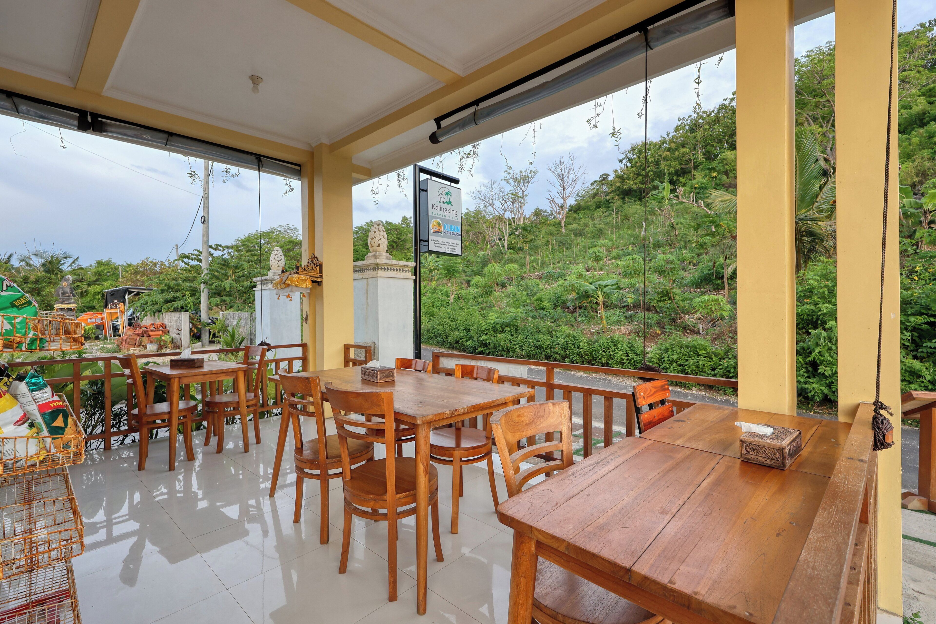 Een restaurant met houten tafels en stoelen, uitzicht op groen en een bord.