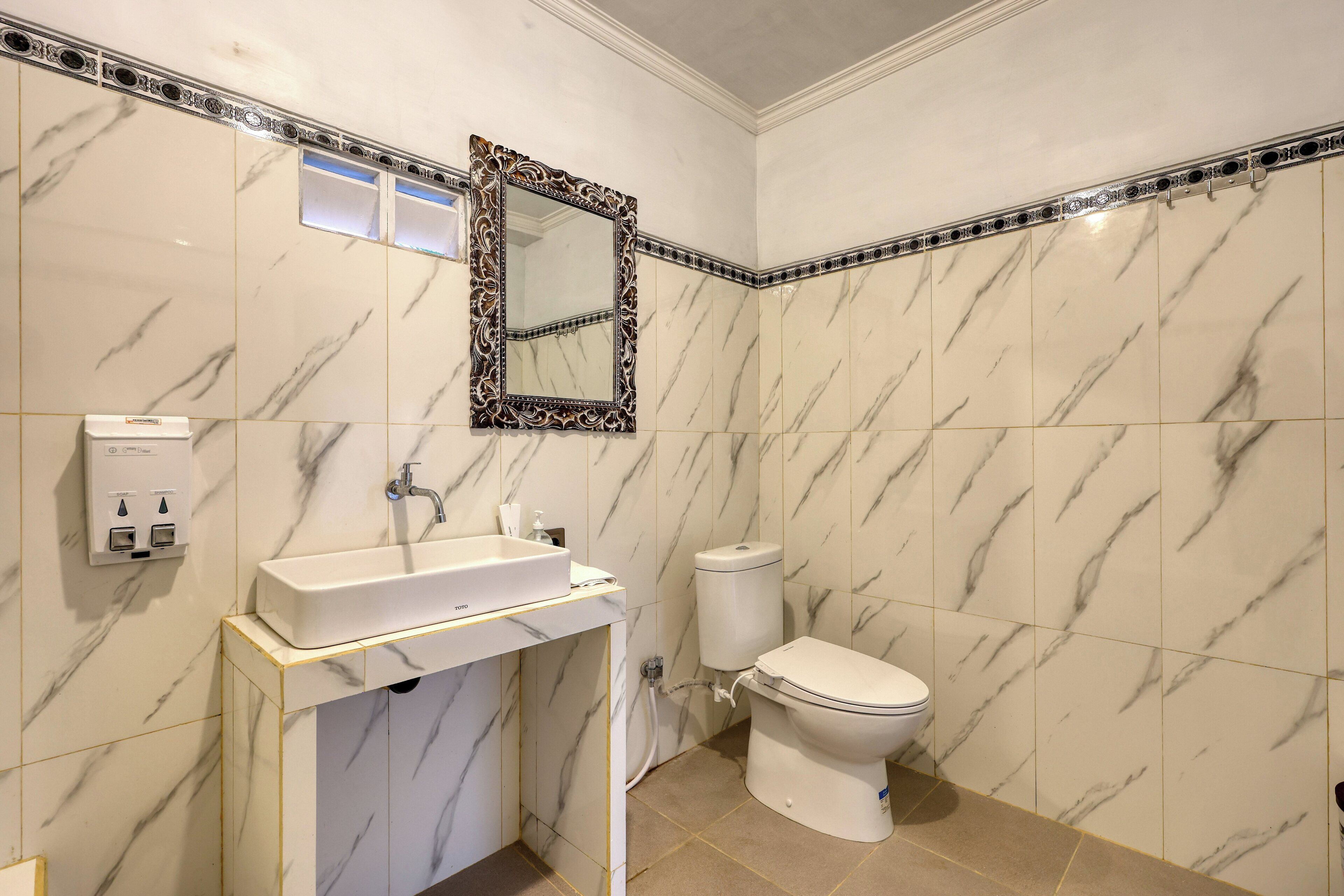 A bathroom with a marble sink, toilet, and a mirror with an ornate frame.