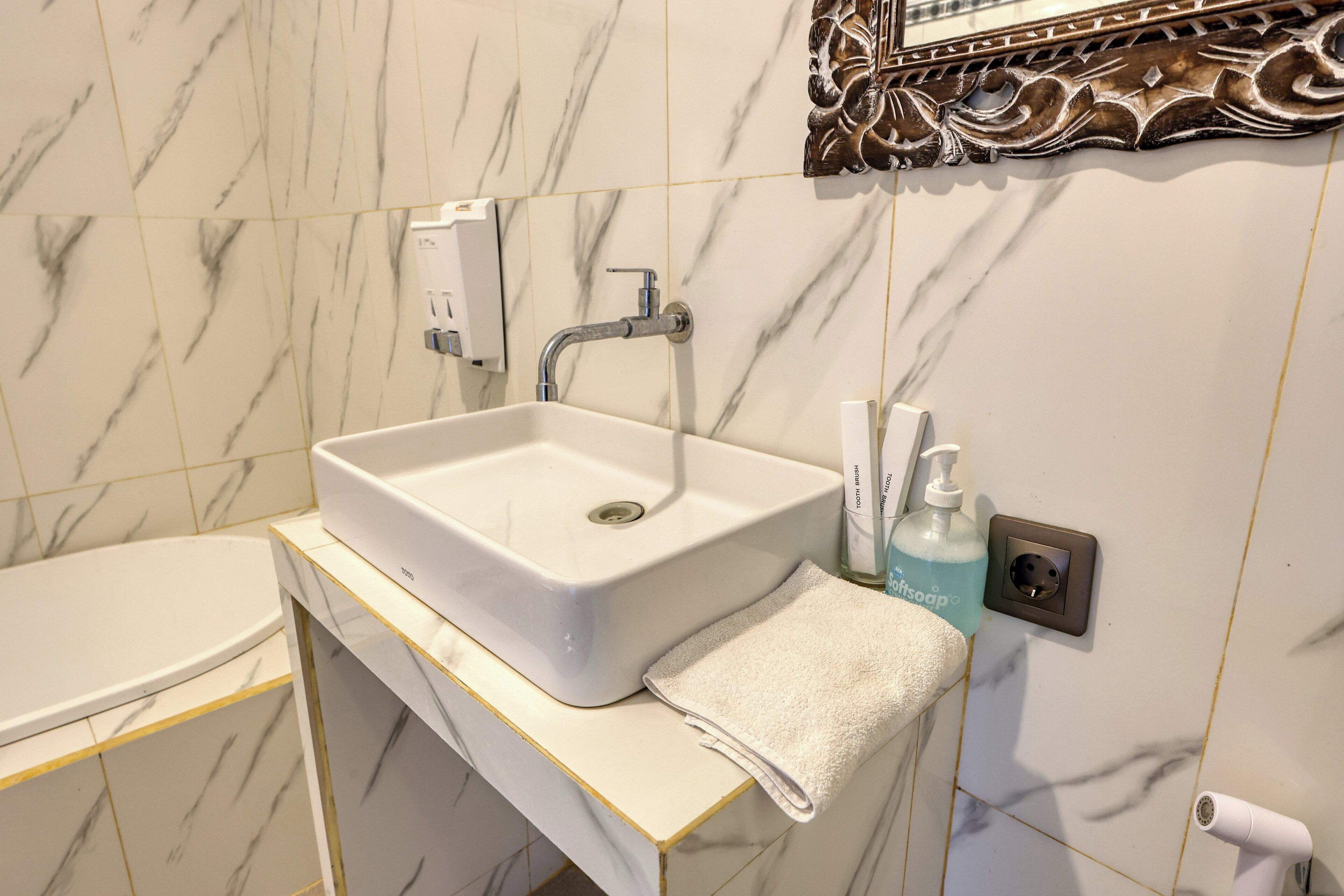 A bathroom with a white sink, a mirror with an ornate frame, a towel, and a soap dispenser.
