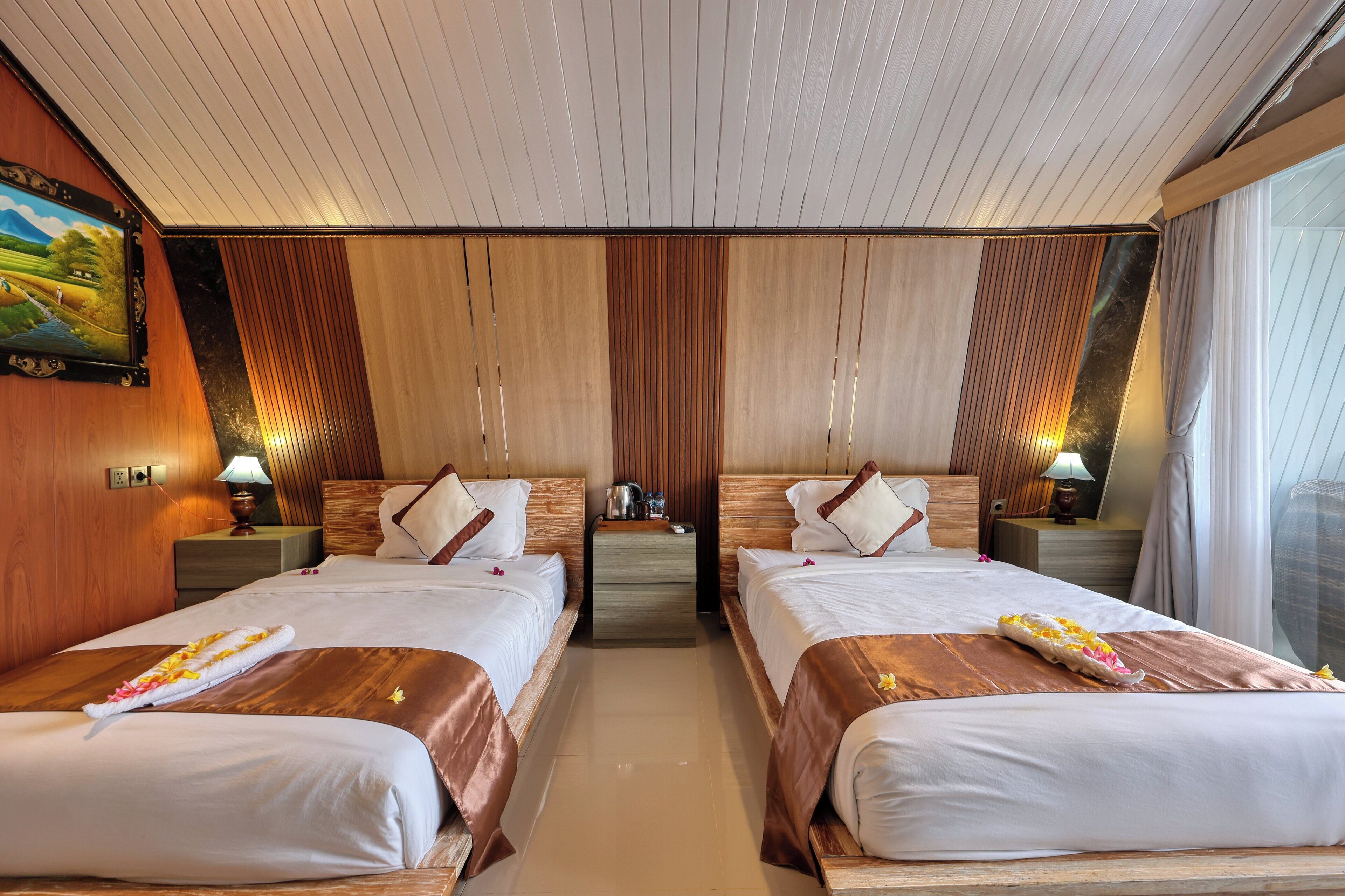 Habitación de hotel con dos camas, cabeceros de madera, un cuadro en la pared y una mesita de noche con una lámpara.