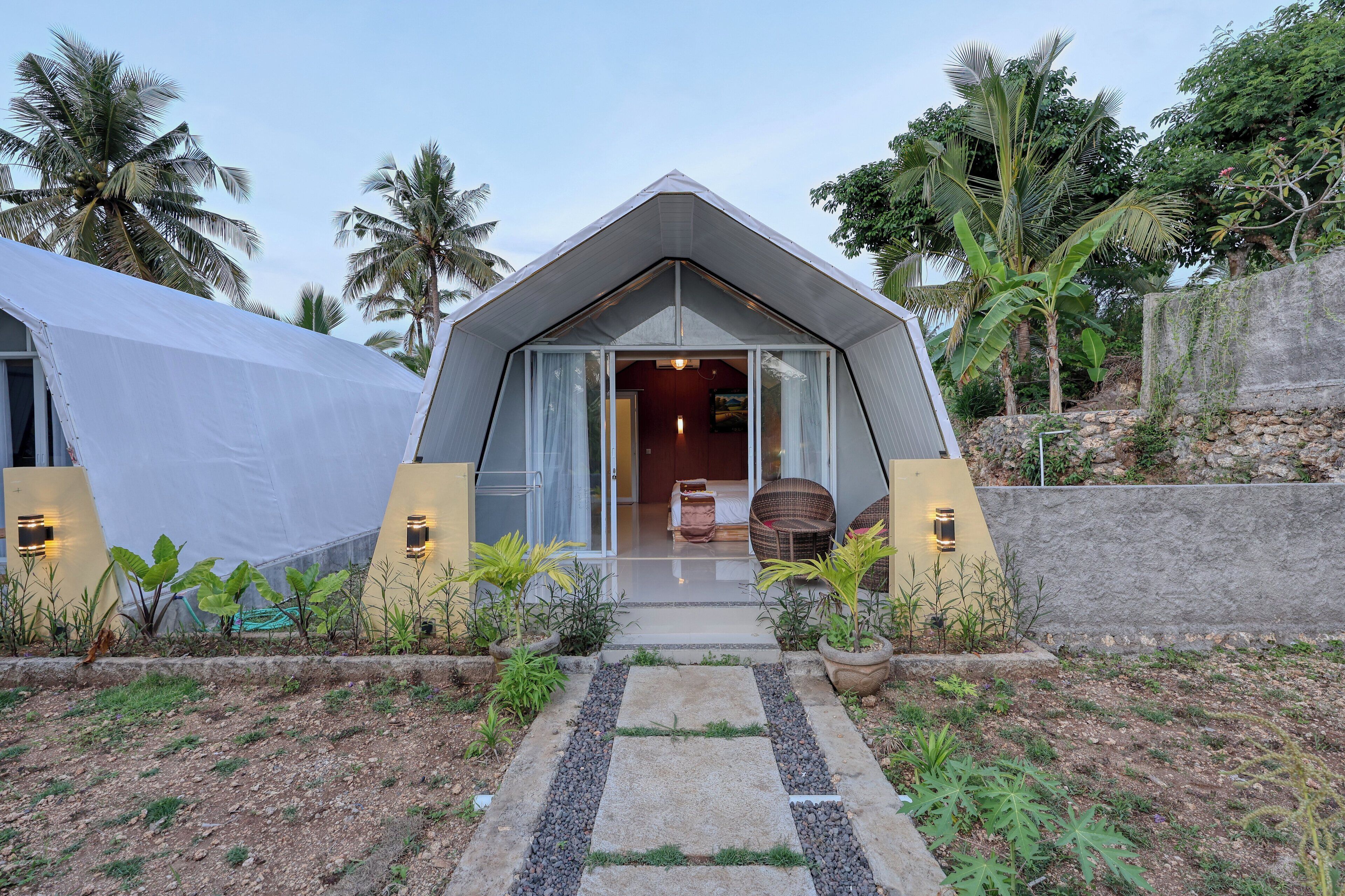 Un edificio moderno de forma triangular con un acceso cubierto y un interior visible con cama y zona de estar.
