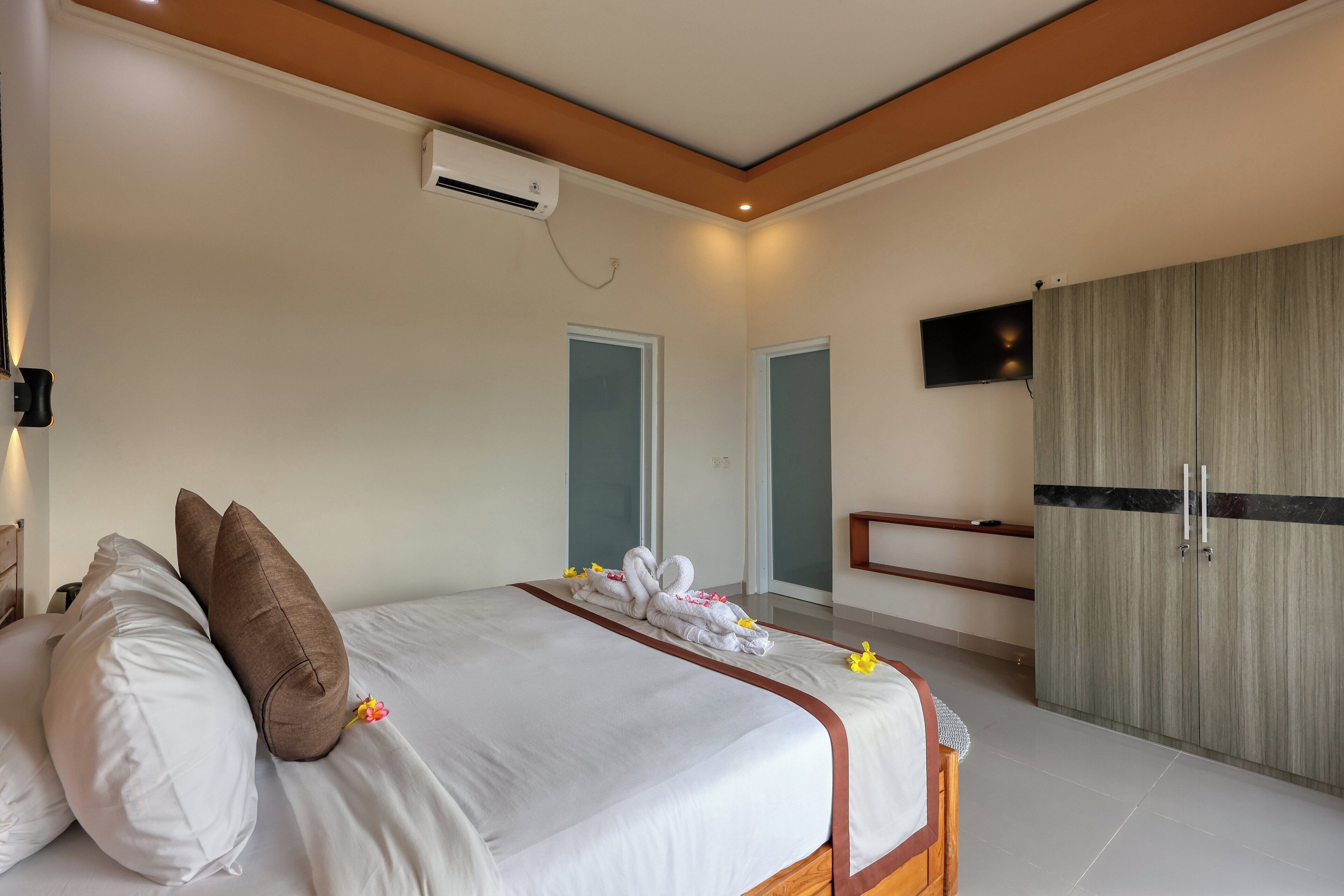 Una habitación de hotel con una cama, almohadas, un televisor y un armario.