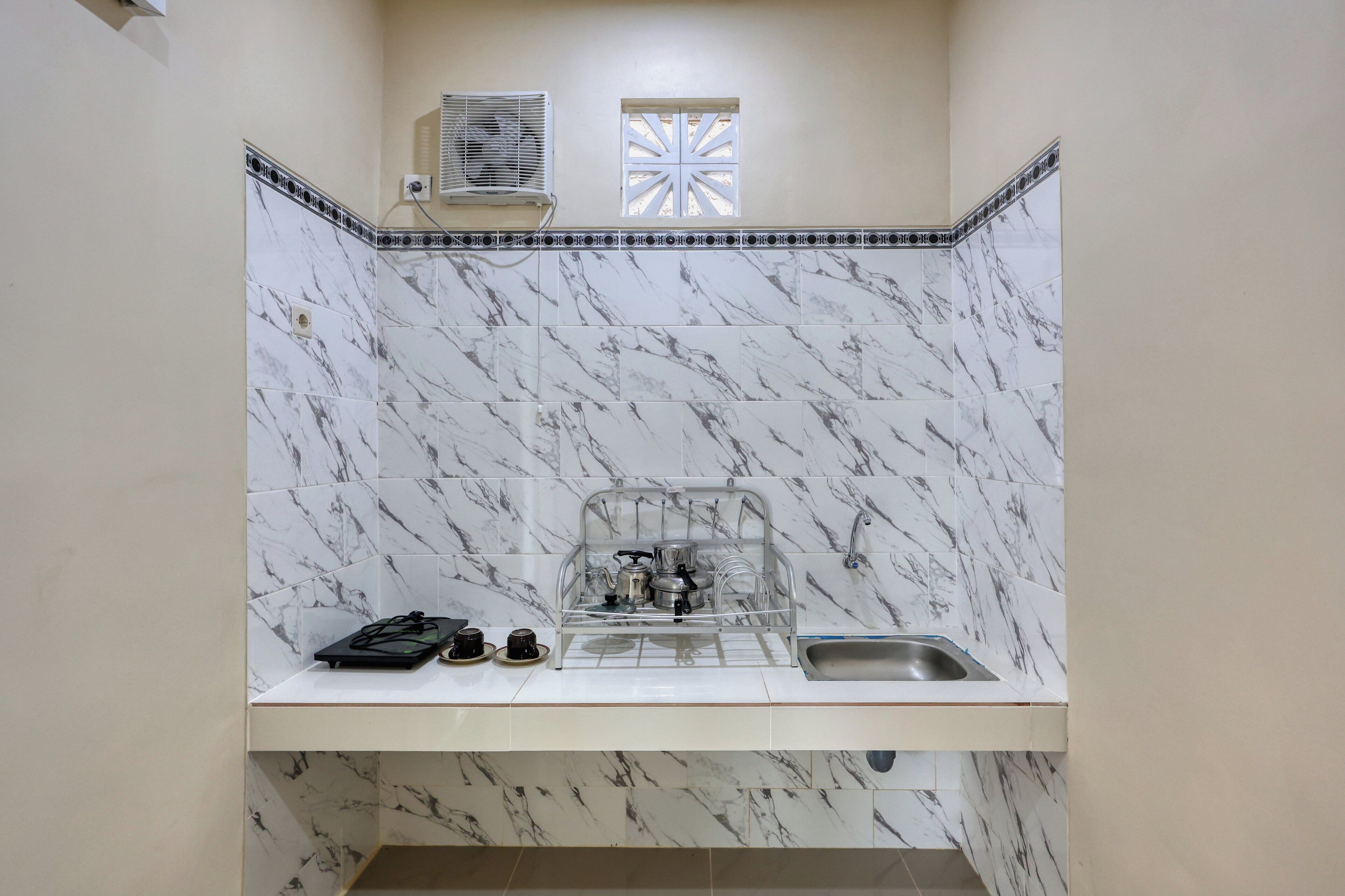 A compact kitchen with marble tiles, a sink, a stove, and a window with a decorative grille.