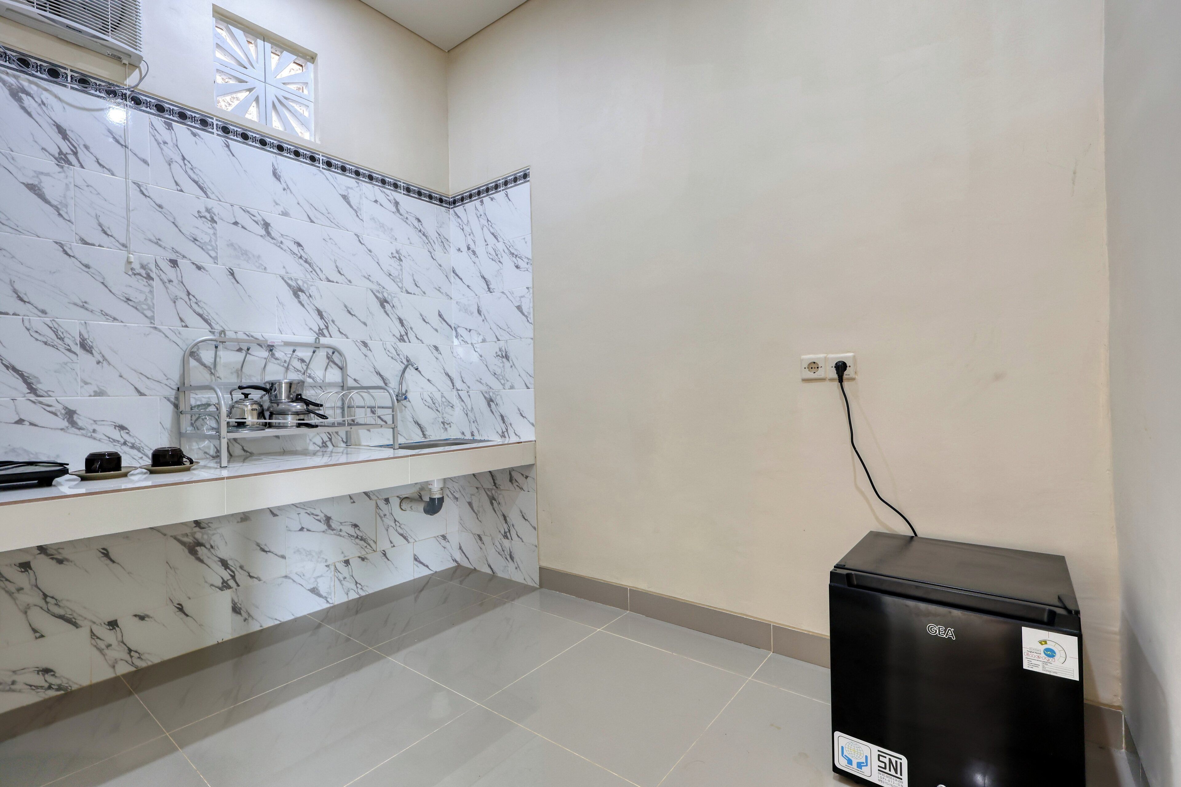 A kitchen with marble tiles, a sink, a countertop with kitchenware, and a black refrigerator.