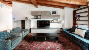 Una sala de estar con televisor, sofás, una mesa de centro y una estantería.