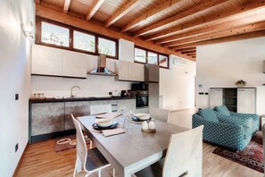 A modern kitchen with wooden beams, a dining area with a table set for two, and a living area with a sofa. - Casarico - MyHomeinComo (Maslianico)