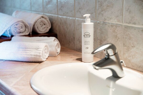 A bathroom with a white sink, a bottle of hand soap, and neatly rolled towels.