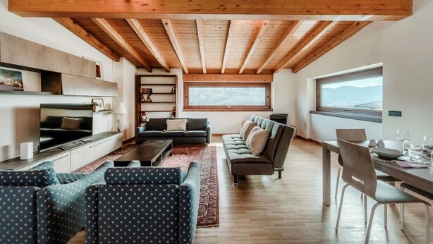 Una sala de estar moderna con televisor, sofás, una mesa de comedor y un amplio ventanal con vistas a la montaña.