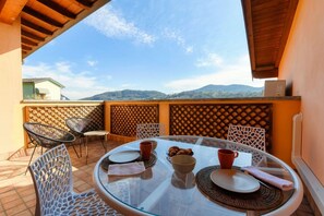 An outdoor dining area with a glass table, wicker chairs, and a view of mountains. - Casarico - MyHomeinComo (Maslianico)