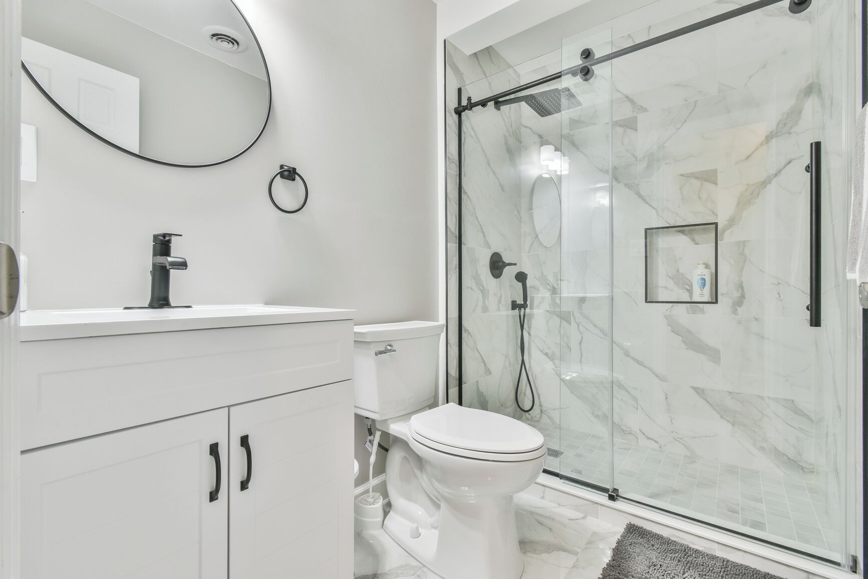 A modern bathroom with a glass-enclosed shower, a white toilet, and a vanity with a mirror and sink.