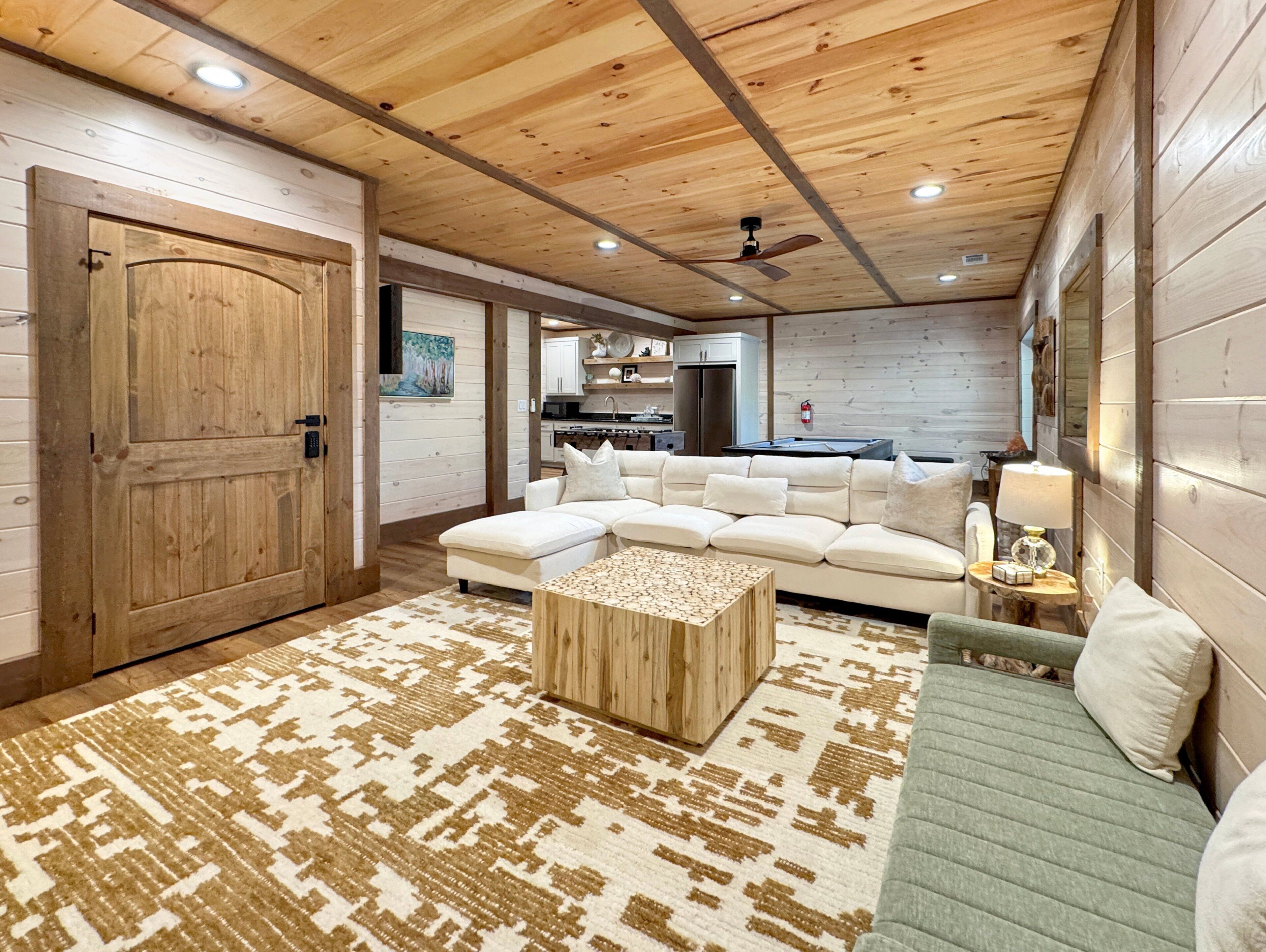 Una sala de estar amplia con techo de madera, un sofá modular grande, una mesa de centro de madera y una alfombra estampada.