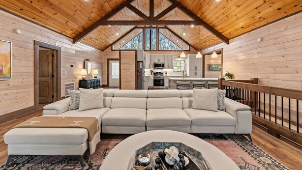 A spacious living room with a large sectional sofa, a fireplace, and a kitchen in the background. - Cardinal Lodge - Elevated Luxury, Minutes From Fun (Mineral Bluff)