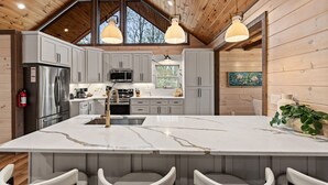 A modern kitchen with a large island, stainless steel appliances, and a wooden ceiling. - Cardinal Lodge - Elevated Luxury, Minutes From Fun (Mineral Bluff)
